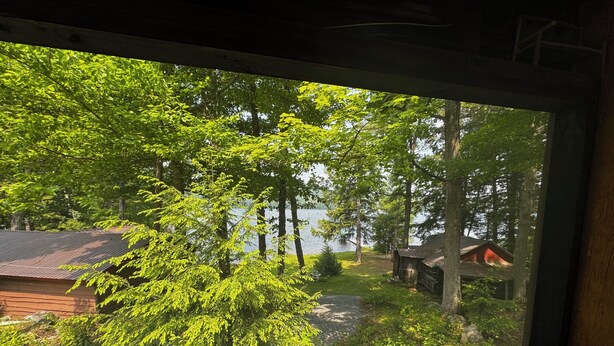Vista desde una ventana de una cabaña, con un lago y un bosque al fondo.