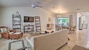 A spacious living room with a sofa, armchairs, a TV, and a dining area with chairs and a table. - Pool Access & Beach Gear! Canalfront Naples Home (Naples)