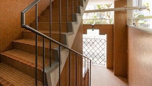 Una escalera con barandilla metálica y escalones de madera, que conduce a un espacio exterior con vistas a árboles y una valla.