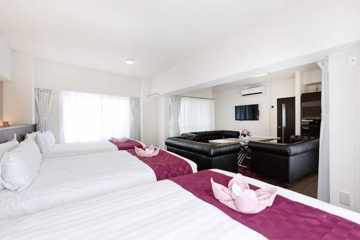 A hotel room with two beds, a sofa, a TV, and an air conditioning unit.