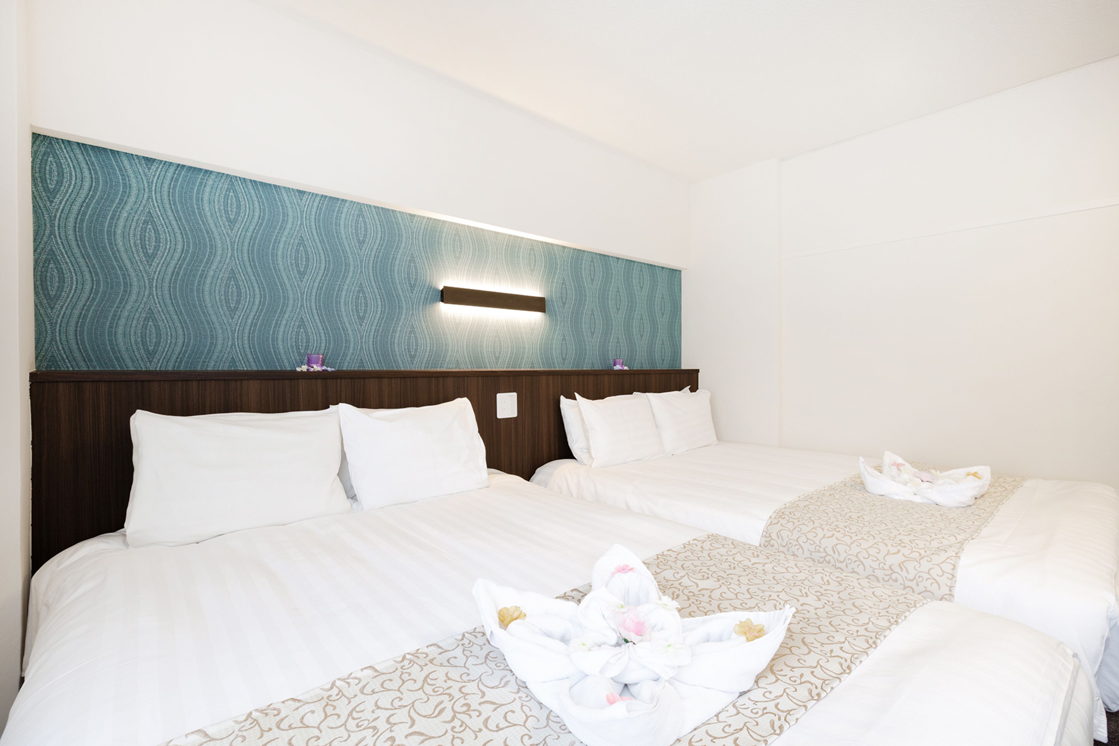 Une chambre d’hôtel avec deux lits, une tête de lit en bois, une lampe fixée au mur et un panneau décoratif mural.