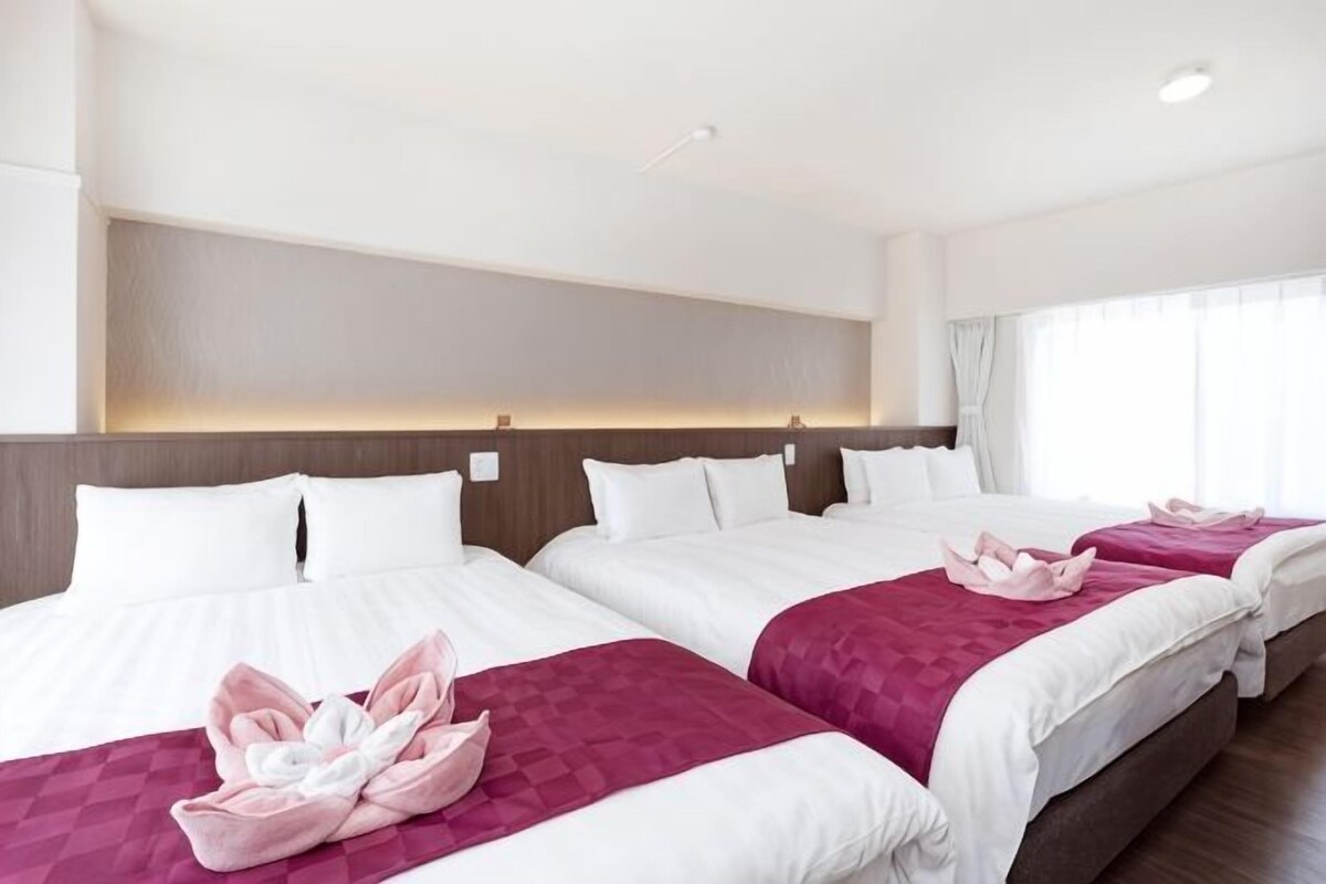 A hotel room with three beds, each with a pink towel and white bedding.