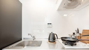 Una cocina moderna con un lavamanos de acero inoxidable, un hervidor, un wok sobre una estufa portátil y armarios de madera.