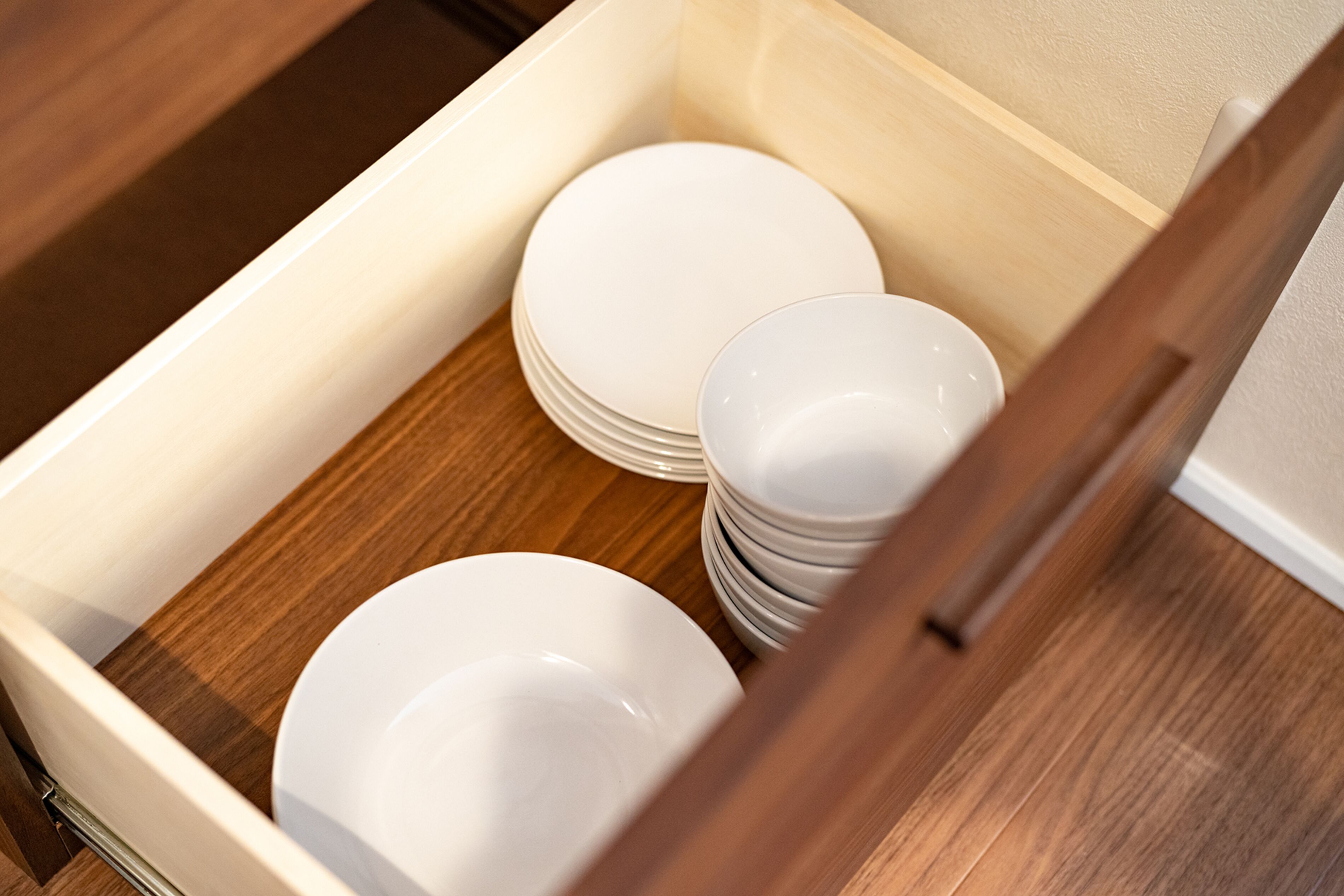 A drawer containing neatly stacked white plates and bowls.