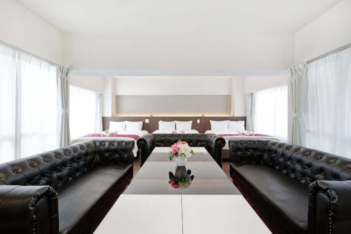 Una habitación con dos sofás de cuero, una mesa central con un florero y una cama con almohadones.