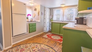 Una cocina compacta con refrigerador, gabinetes verdes, un lavamanos y una ventana.