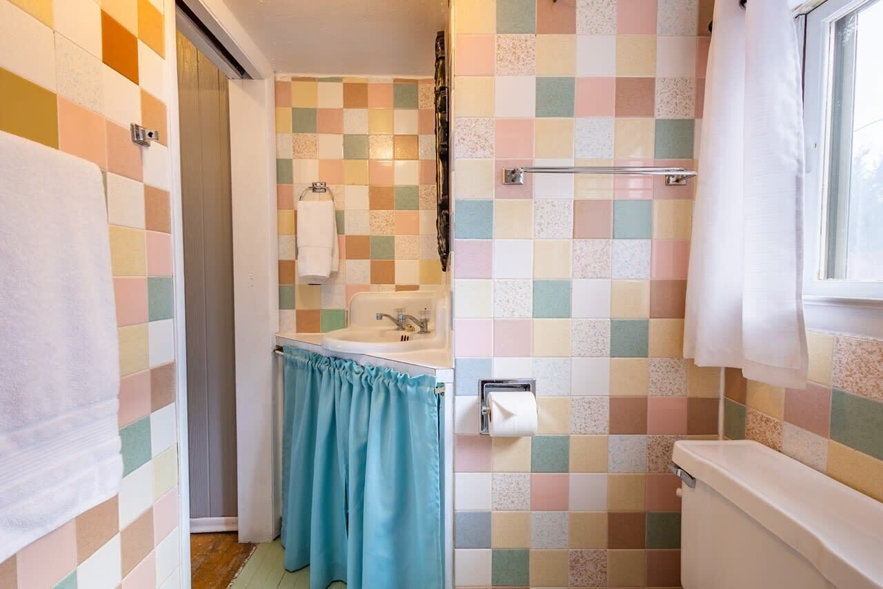 Une salle de bain avec un mur recouvert de carreaux à motifs géométriques, un lavabo, des toilettes et une fenêtre.