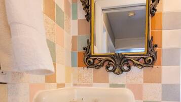 A bathroom with a checkered tile wall, a white sink with a decorative mirror above it, and a blue curtain.