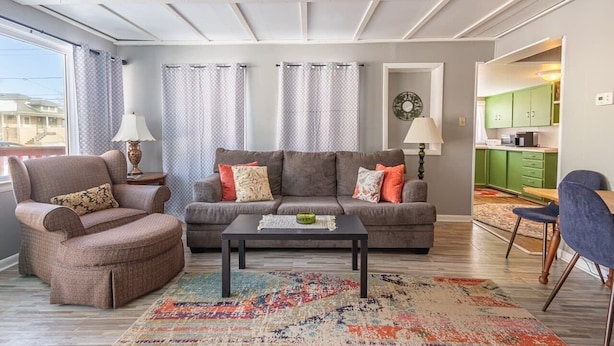 Una sala de estar con sofá, sillón, mesa de centro y alfombra estampada.
