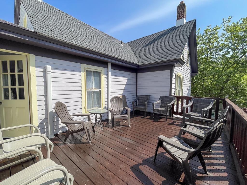 A deck with outdoor furniture, including chairs and a table, and a house with white siding and a dark roof.