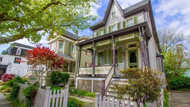 Una casa de estilo victoriano con un porche, cerca de piquete y un jardín bien cuidado.