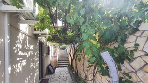 Un sendero empedrado que lleva a una escalera, rodeado de un muro de piedra y abundante vegetación.