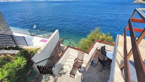 Una propiedad costera con vistas despejadas al mar, una escalera que lleva a una terraza y mobiliario de exterior.