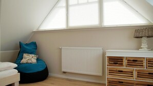 A room with a sloped ceiling, a white radiator, a wooden storage unit, and a bean bag with pillows. - Semi-detached house - Isabella - Bright vacation home spread over 3 floors with (Zingst)