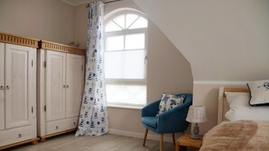 A bedroom with a bed, a chair, a lamp, a wardrobe, and a window with a curtain. - Semi-detached house - Isabella - Bright vacation home spread over 3 floors with (Zingst)