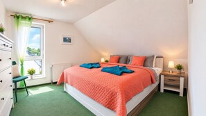 Une chambre à coucher comprenant un lit, une table de chevet, une commode, une fenêtre donnant sur un paysage agréable et un radiateur.
