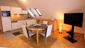 A compact kitchen with modern appliances, a dining area with a table and chairs, and a flat-screen TV. - Apartment Jonathan - Modern equipped apartment near the center! (Zingst)