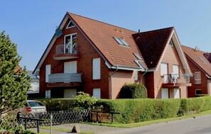 Une maison à deux étages, construite en briques, avec un toit en pente, un balcon au premier étage et un petit jardin.