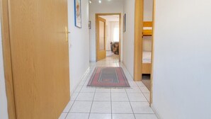 Un couloir étroit, avec une porte en bois sur la gauche, un lit superposé sur la droite et un sol carrelé.