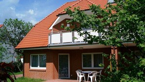 Une maison à deux étages, avec un toit recouvert de tuiles rouges, un balcon et une petite terrasse agrémentée d’une table et de chaises.