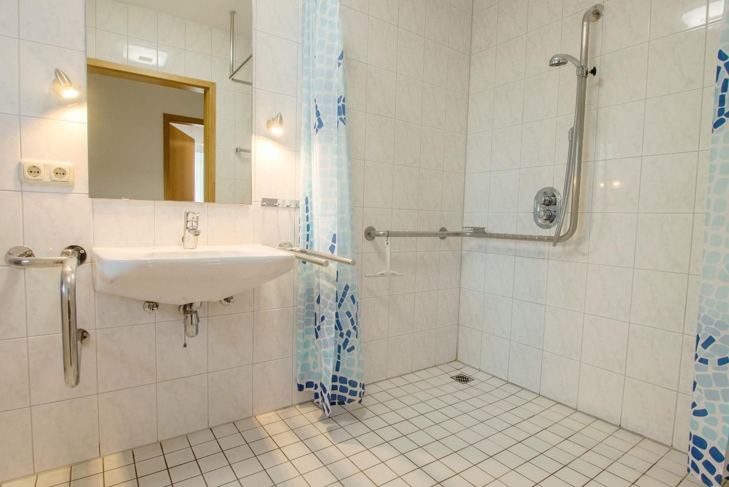 A bathroom with a white sink, a mirror, a shower with a glass door, and tiled walls.
