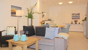A modern living room with a sofa, a coffee table, and a dining area with a table set for two. - Modern 3-room apartment directly behind the Baltic Sea dike - Logierhaus Friedrich (Zingst)