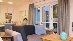 A modern living room with a grey sofa, a wooden coffee table, and a dining area with a table set for two. - Modern 3-room apartment directly behind the Baltic Sea dike - Logierhaus Friedrich (Zingst)