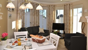 Ein gemütliches Wohnzimmer mit einer schwarzen Couch, einem Esstisch, der für ein Frühstück gedeckt ist, und einem Flachbildfernseher.