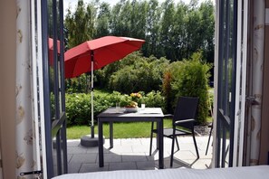 Un patio al aire libre con una mesa, un paraguas rojo y una silla.