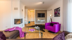 A modern living room with a fireplace, a glass coffee table, a purple sofa, and a leather couch. - Exclusive vacation apartment in Zingst: 132 m² of comfort right on the Baltic Sea beach - (Zingst)