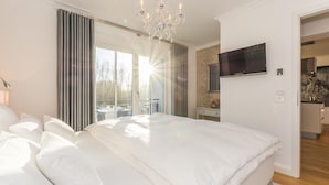 Un dormitorio amplio con una cama grande, una araña, un televisor y vistas al exterior.
