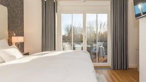 Un dormitorio moderno con una cama grande, una mesita de noche, una lámpara y un balcón con mesa y sillas.