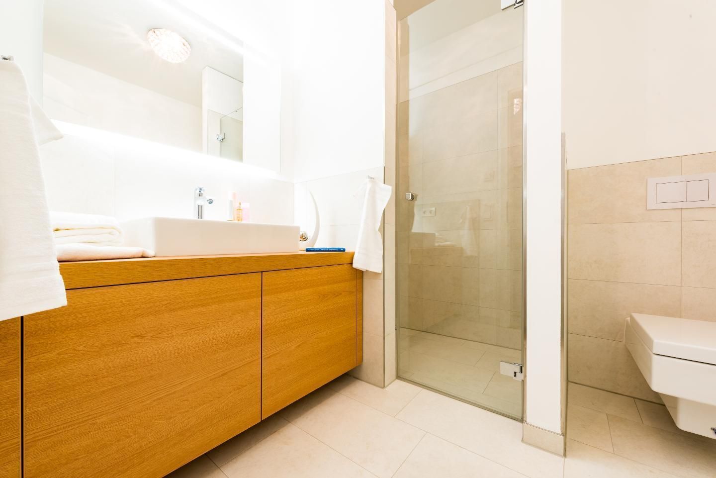 A modern bathroom with a wooden vanity, a glass shower enclosure, and a white toilet.
