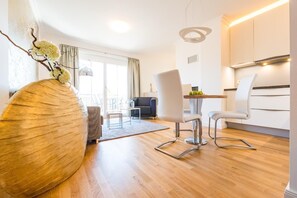 Un soggiorno moderno con una grande scultura in legno, una zona pranzo con tavolo e sedie, e una cucina con pensili bianchi e una lampada a sospensione.