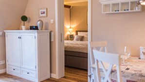 A bedroom with a bed, bedside table, lamp, and a small cabinet. - Exclusive vacation apartment with limited sea view and balcony in Zingst - (Zingst)