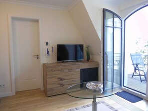 Una sala de estar moderna con un televisor sobre un mueble de madera, una mesa de vidrio con un cuenco y un ventanal corredero que da a un espacio exterior.
