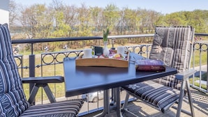 Een balkon met een ontbijttafel, inclusief een boek, een vaas met bloemen en een koffiekop.