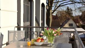Un balcon avec une table préparée pour le petit-déjeuner, comprenant un bol de fruits et un verre de jus d’orange.