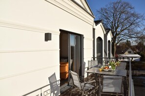Un edificio bianco con un balcone, un tavolo apparecchiato con sedie, una ciotola di frutta e un vaso di fiori.