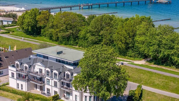 Un bâtiment moderne à deux étages, doté d’un toit plat et de grandes fenêtres, situé près d’un front de mer, avec une jetée qui s’avance dans l’eau.