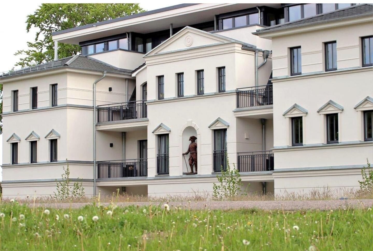 A multi-story residential building with balconies and a statue on the ground floor.