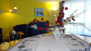 Sala de estar com um sofá azul, um vaso com flores vermelhas e um quadro na parede.