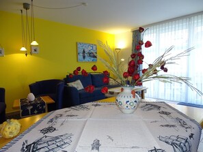 Un salon avec un canapé bleu, un vase rempli de fleurs rouges et un tableau accroché au mur.