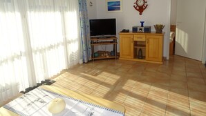 Sala de estar com televisão, aparador de madeira e porta para outro cômodo.