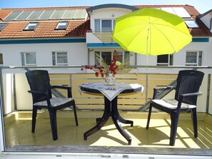 A balcony with two chairs and a table, a yellow umbrella, and a vase with red flowers. - Comfortable vacation apartment in first beach row with balcony in Zingst - Residence (Zingst)