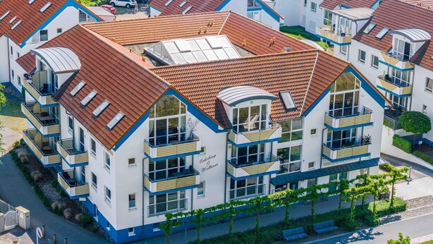 A modern multi-story residential building with a red-tiled roof, balconies, and a central courtyard. - Comfortable vacation apartment in first beach row with balcony in Zingst - Residence (Zingst)