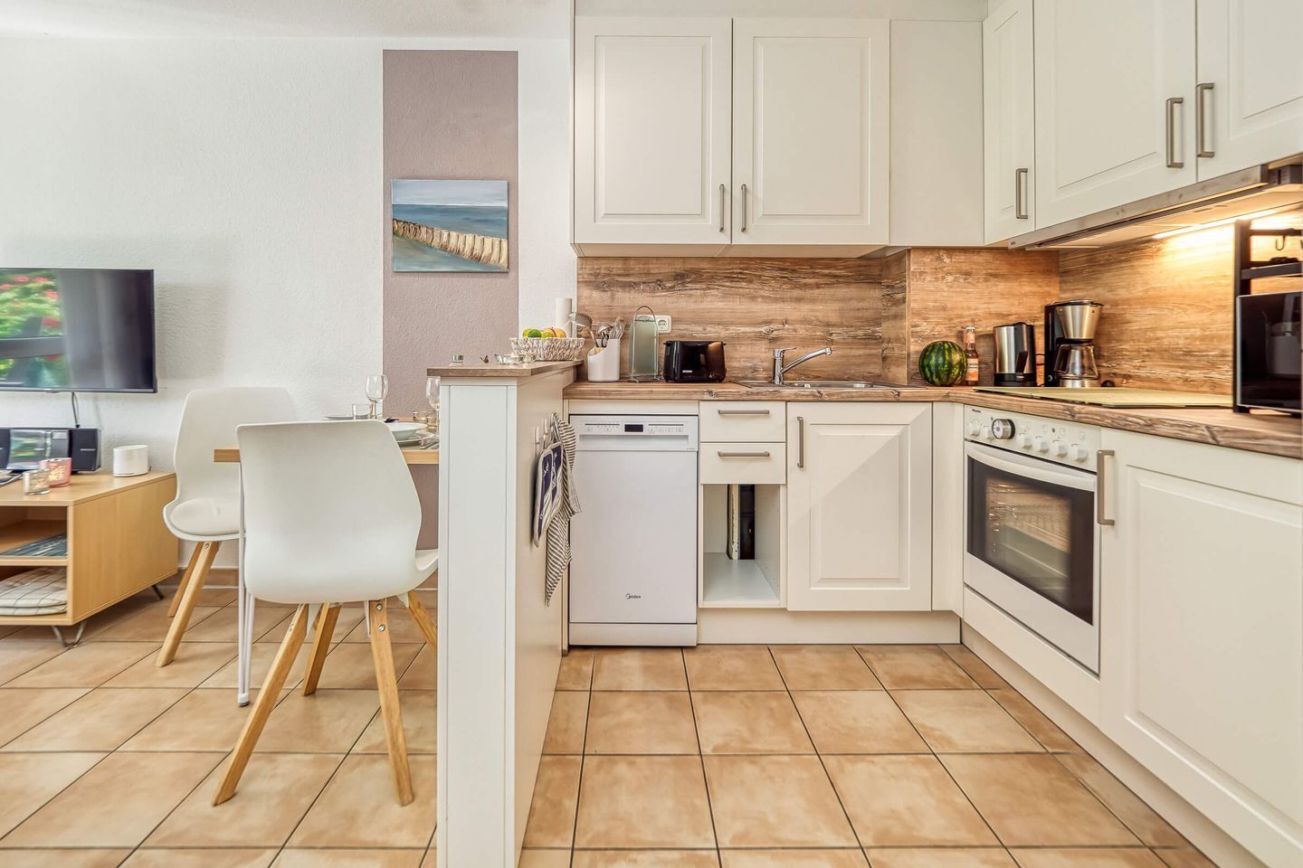A modern kitchen with white cabinets, a dishwasher, an oven, and a microwave. There is a dining area with a table and chairs.