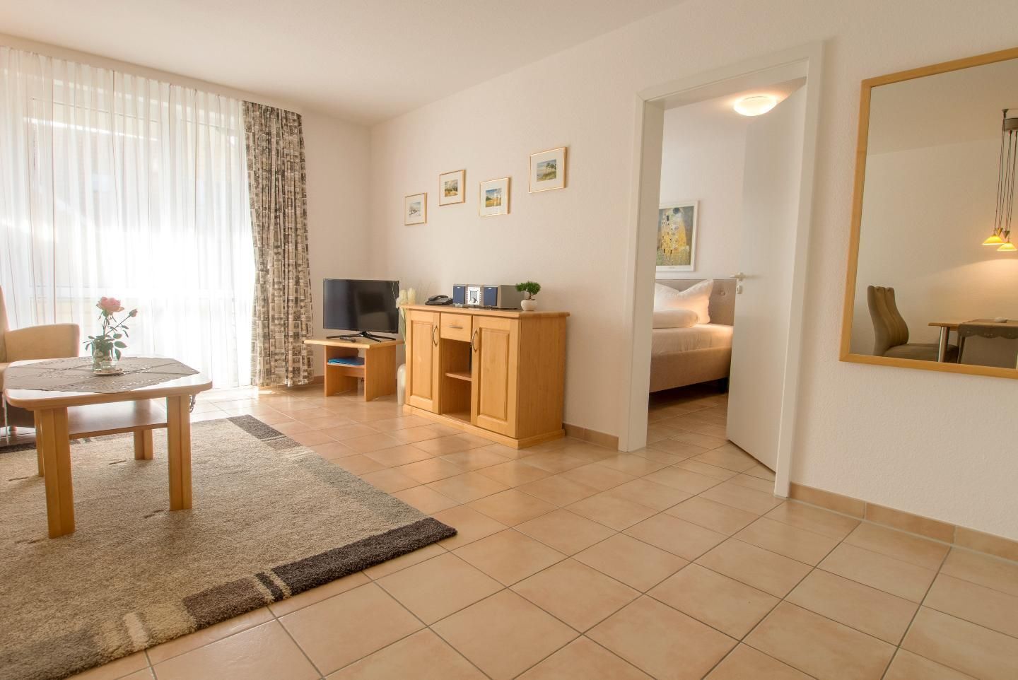 Un saló modern amb zona de menjador, televisió, armaris de fusta i un llit a l'habitació contigua.