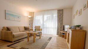 Ein Wohnzimmer mit einer Couch, einem Couchtisch und einer Fernsehecke mit einer Pflanze.