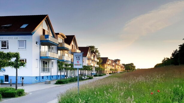 En række traditionelle europæiske huse med balkoner, en klar vej og en græsplæne.